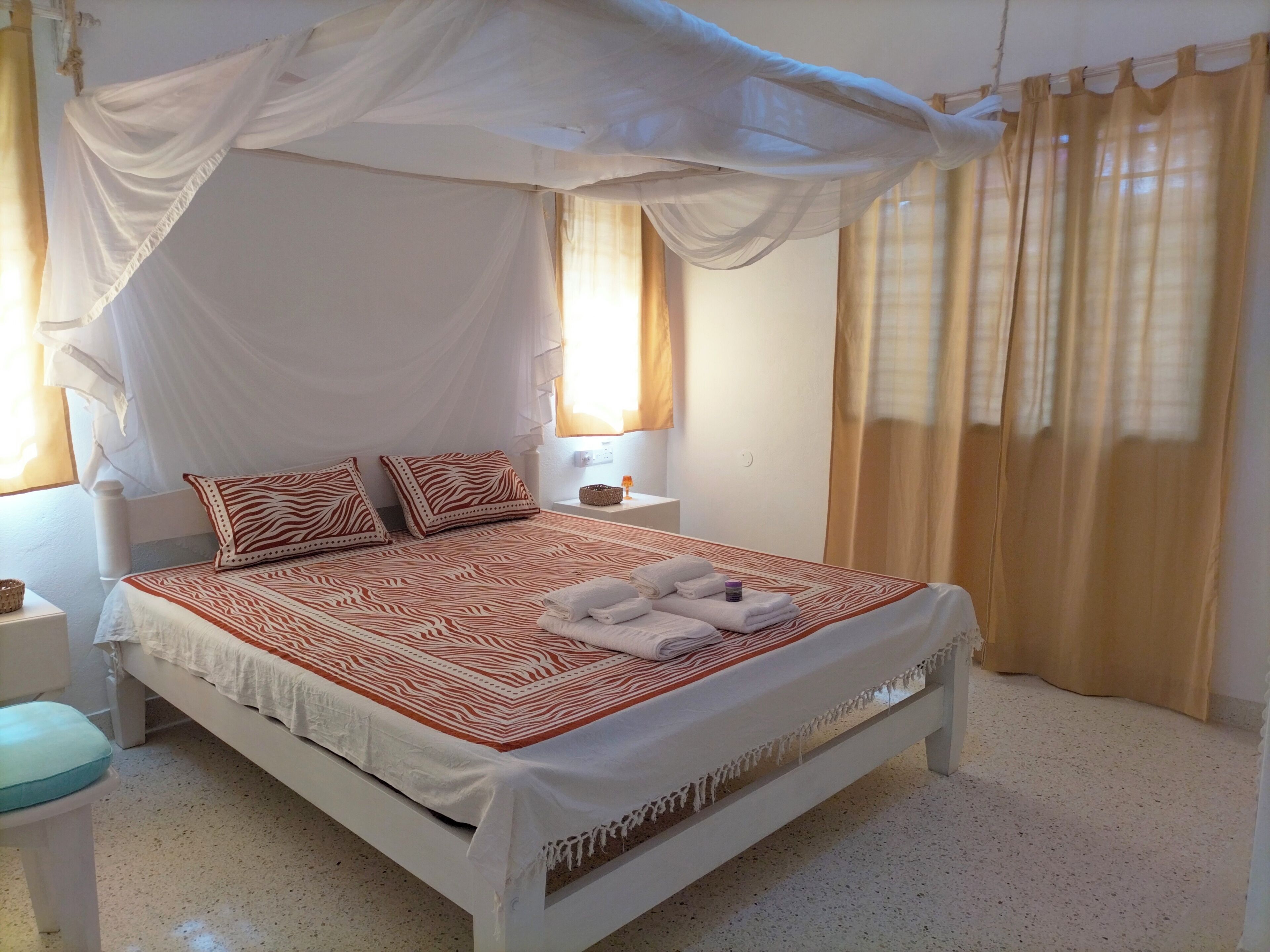 Ein Bett mit Baldachin, zwei Kissen, ein Nachttisch und ein Fenster mit Vorhängen.