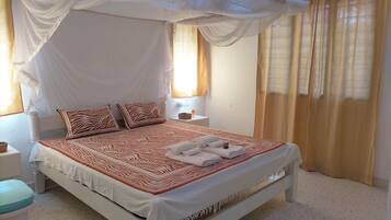 A bed with a canopy, two pillows, a bedside table, and a window with curtains.