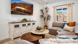 A living room with a sofa, a coffee table, a cabinet, a large painting, and a potted plant. - Skyline 1742, Private Spa, Fire Pit, Community Amenities! (Washington)