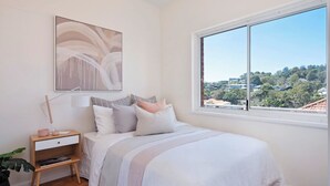 Ein Schlafzimmer mit Bett, Nachttisch, Lampe und einem großen Fenster mit Blick.