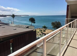 A balcony with a view of the ocean, a beach, and a distant shoreline. - Bower st Ocean View Retreat (Manly)