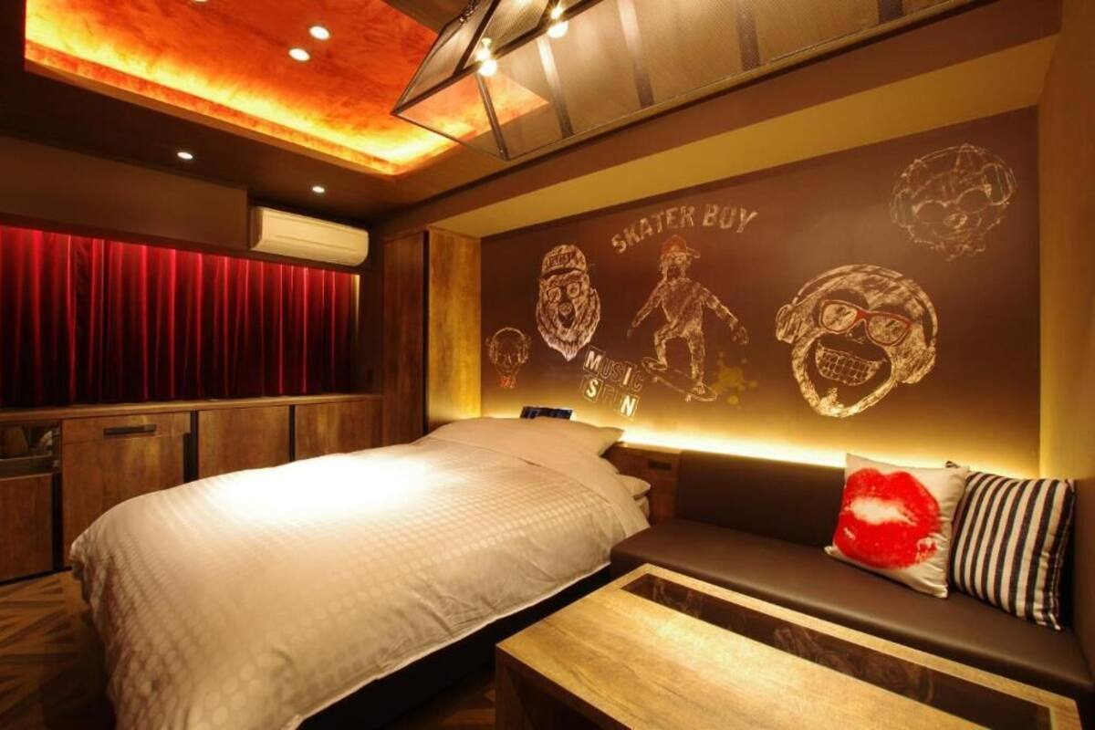 Une chambre d’hôtel avec un lit, un coin salon agrémenté d’un coussin en forme de cœur rouge, et un mur décoré de motifs sur le thème du skateboard.