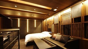 A modern hotel room with a bed, a sofa, a desk, and built-in wooden paneling.