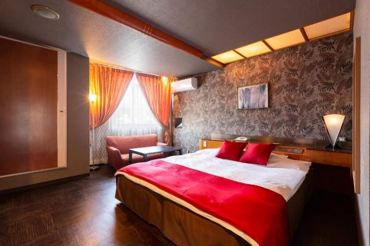 A hotel room with a large bed, a desk, a chair, a window with curtains, and a patterned wall.