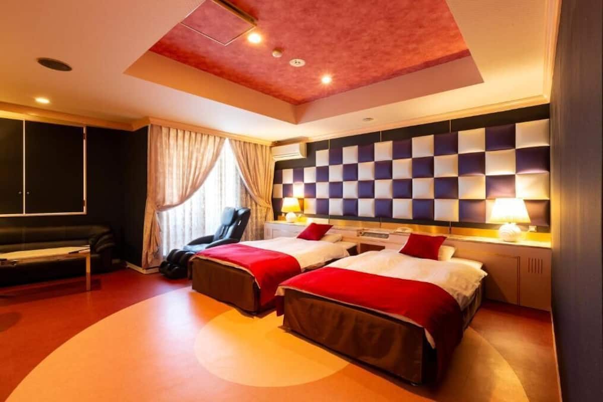 A hotel room with two beds, a sofa, a desk, and a large window with curtains.