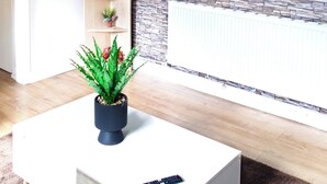 Un salón con una pared de diseño de piedra, un televisor montado que muestra 'NETFLIX', una mesa de centro blanca con una planta en maceta y una estantería con objetos decorativos.