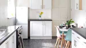 Una cocina moderna con armarios blancos, encimera negra y una zona de comedor con mesa y sillas.