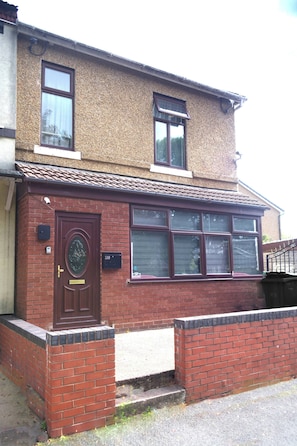 A two-story brick house with a front door, a window with a shutter, and a small porch area. - Elegant 5-bedroom Home- Fast Wifi, Free Parking & Netflix (Wolverhampton)