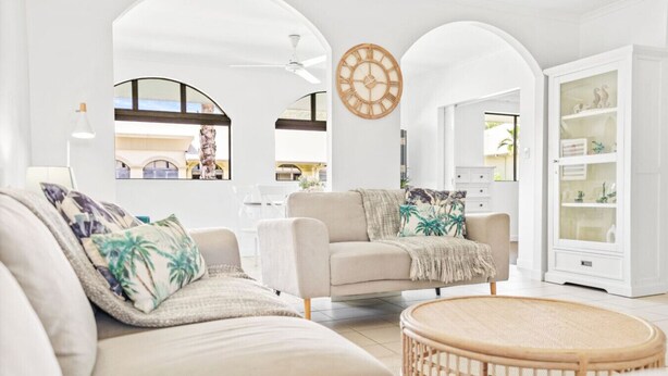 Una sala de estar con sofá, sillón y una mesa de centro redonda, paredes blancas y un reloj de madera.