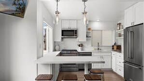 Une cuisine moderne avec des meubles blancs, un grand îlot central doté de tabourets, des appareils en acier inoxydable et un éclairage suspendu.