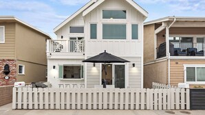 Une maison à deux étages avec un balcon, une clôture blanche en bois et un parapluie noir.