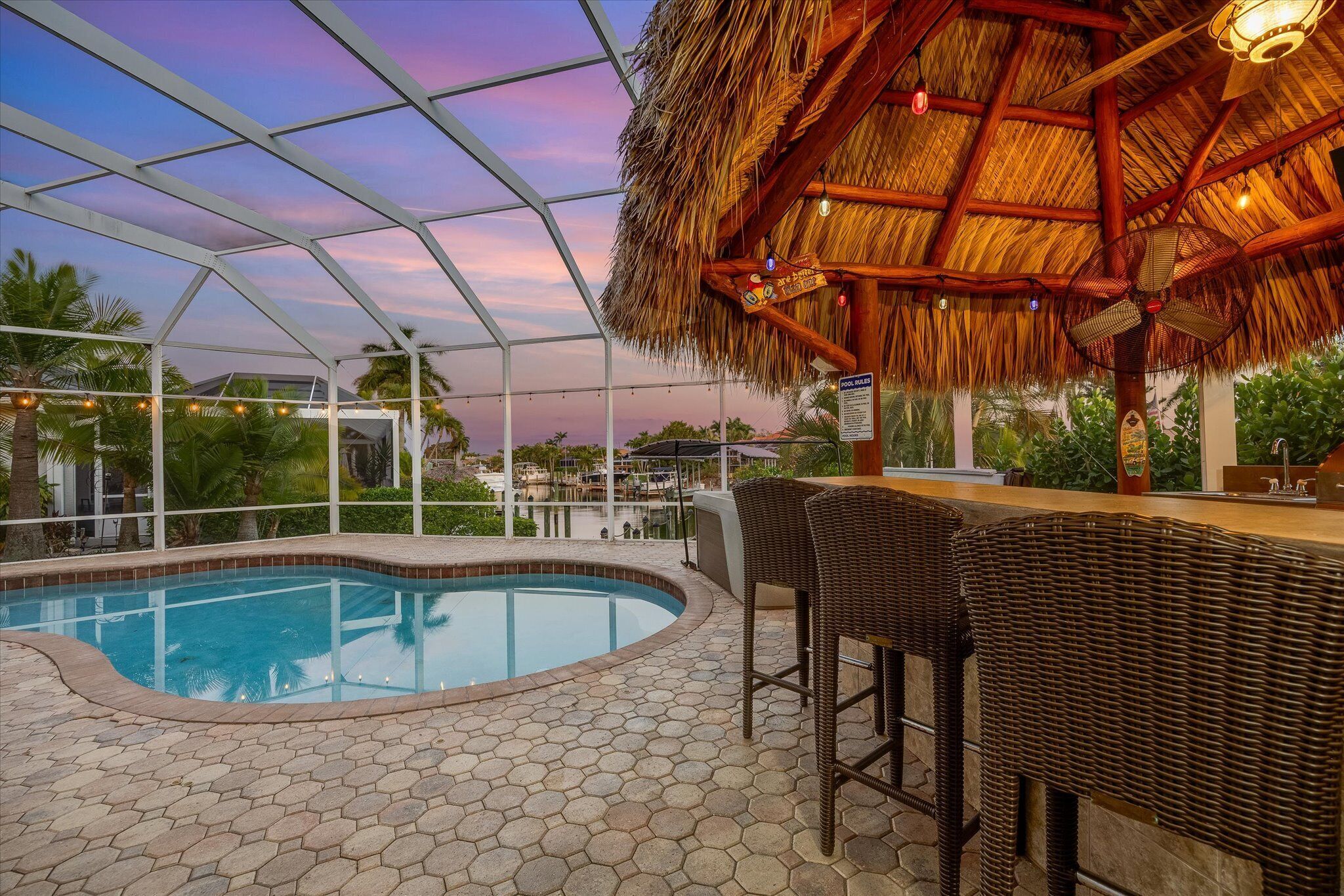 A pool area with a thatched roof, wicker chairs, and a bar.
