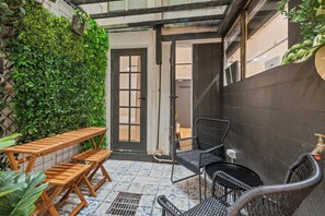Eine Terrasse mit Holztisch und -stühlen, eine schwarze Wand mit Bepflanzung und ein Fliesenboden.