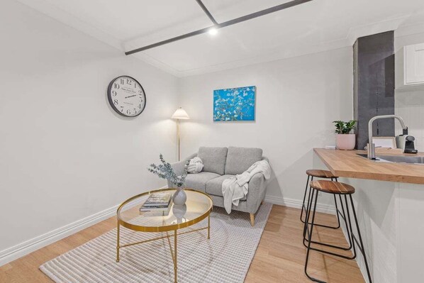Uma sala de estar moderna com um sofá, uma mesa de centro redonda, um relógio, um abajur e um quadro na parede.