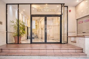 Ein Hotel Eingang mit Glastür, Zimmerpflanze und einem Schild mit der Aufschrift 'The New Yorker'.