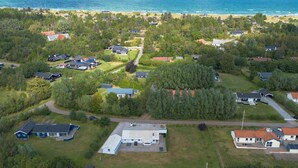 Vue aérienne d’un quartier résidentiel avec des maisons, un grand immeuble et une plage en arrière-plan.