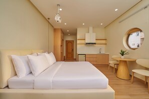 A modern hotel room with a large bed, a small kitchenette, a round dining table, and a window with blinds. - Dalat Blanc Residence (Cam Ly - Da Lat)