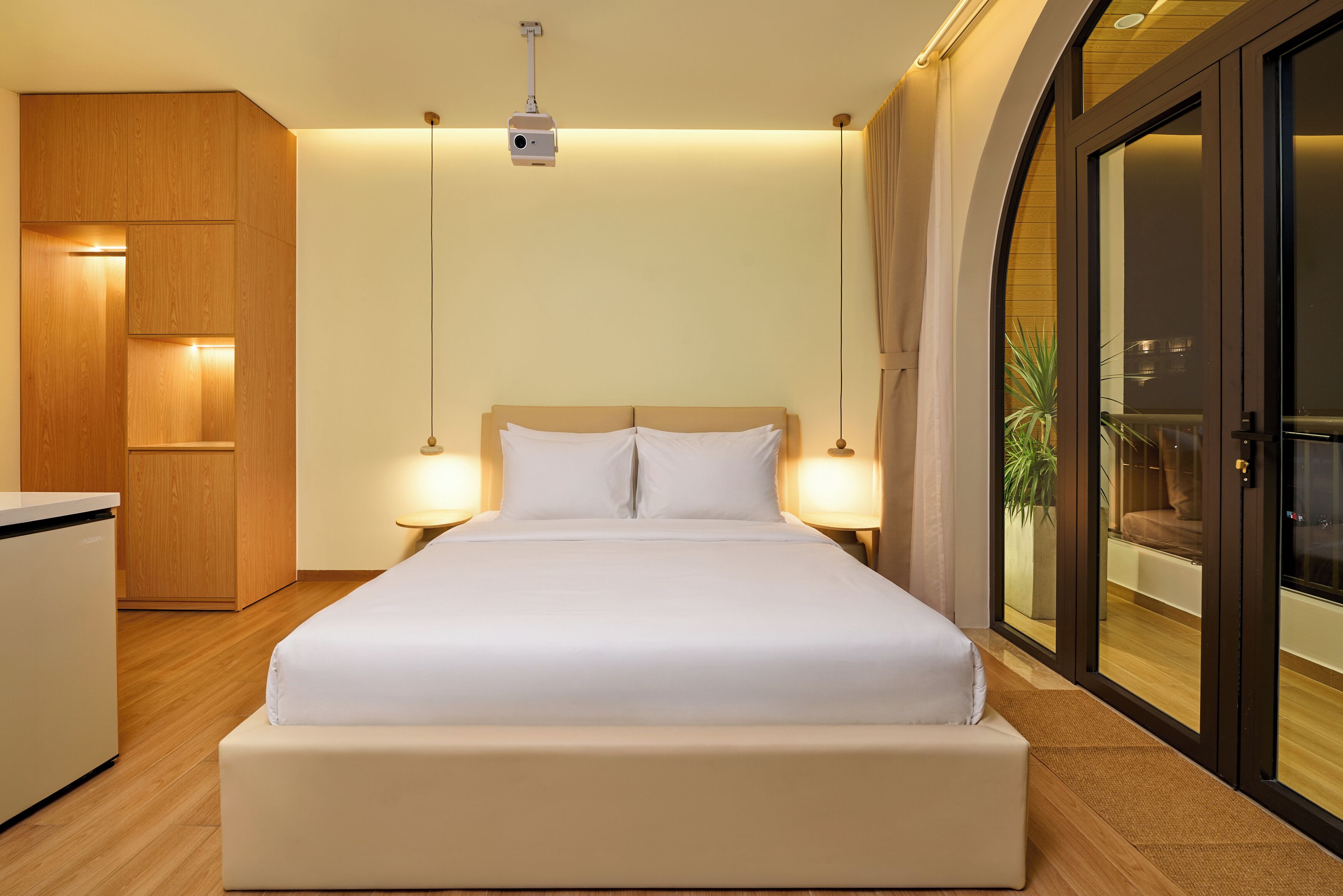 A hotel room with a bed, bedside lamps, a wardrobe, and a sliding glass door to a balcony.