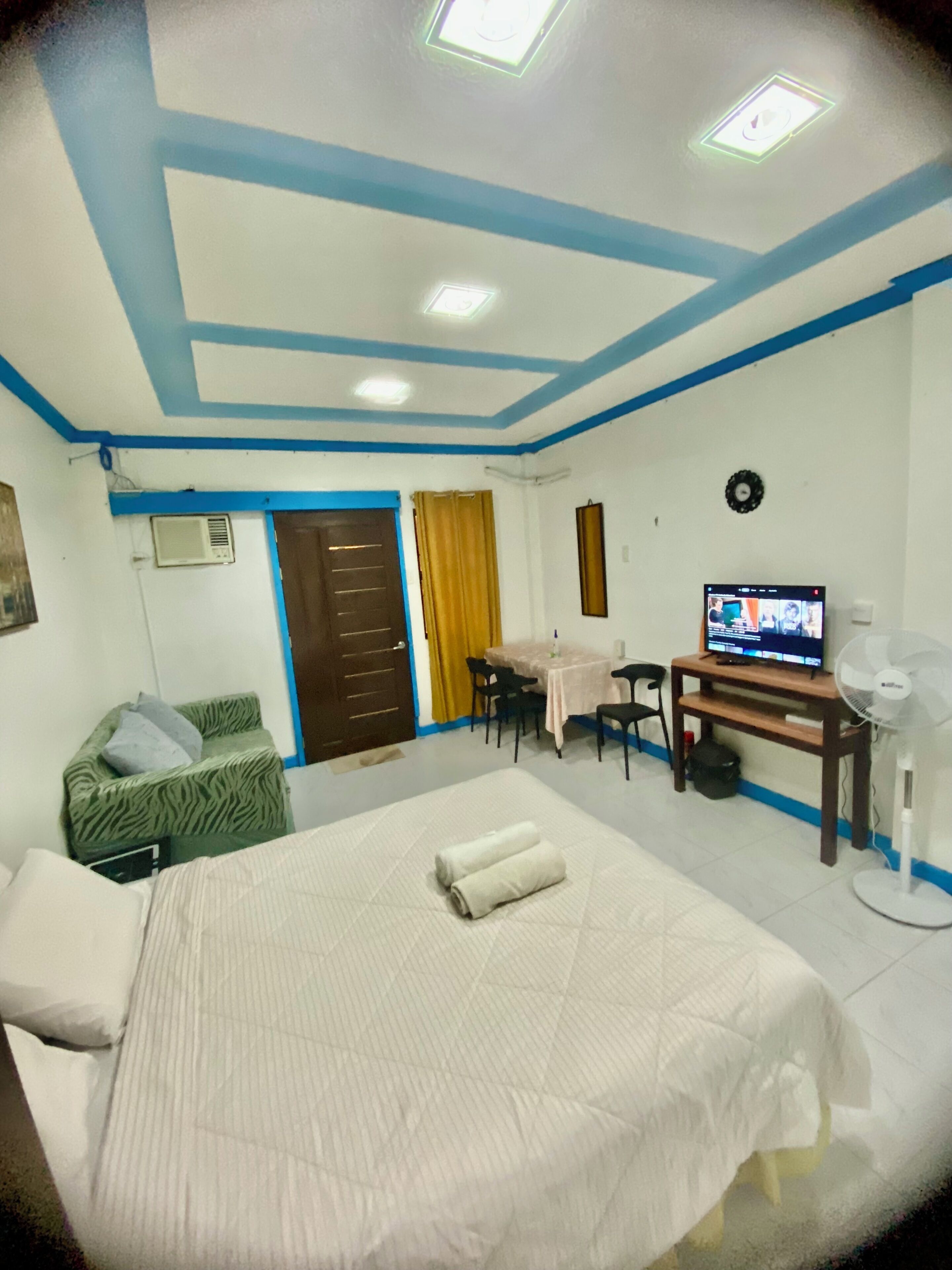A hotel room with a bed, a desk, a television, and a fan.