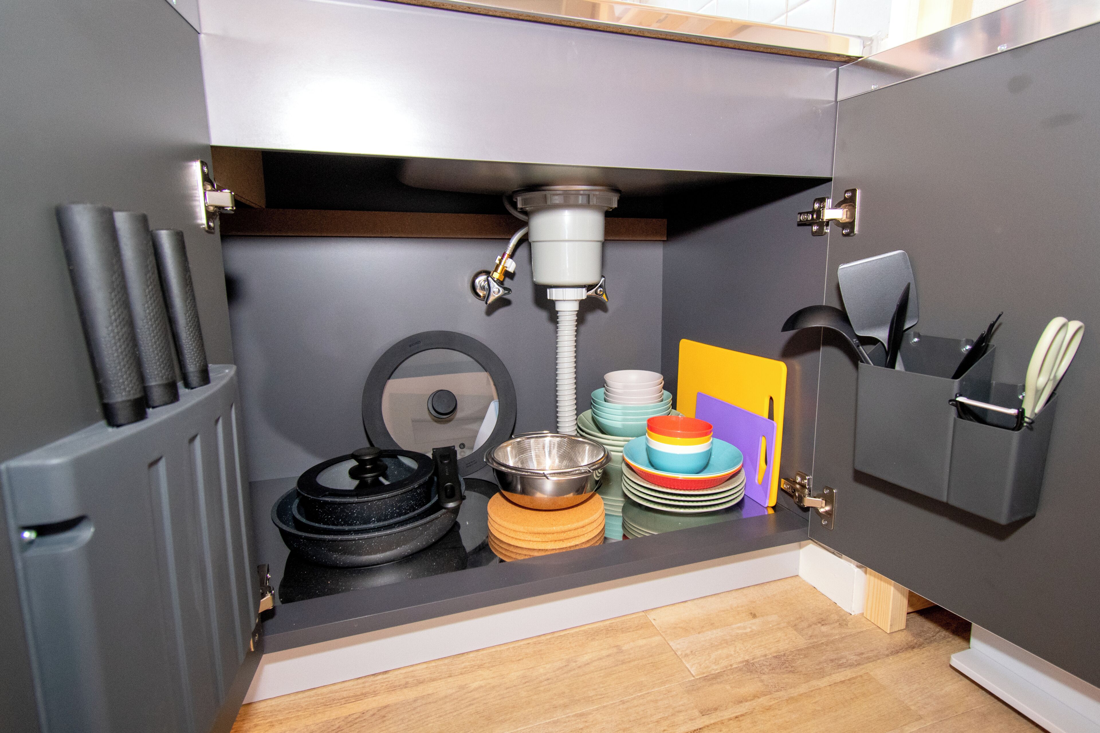 A kitchen with a sink, a dish rack, and a cabinet with utensils.