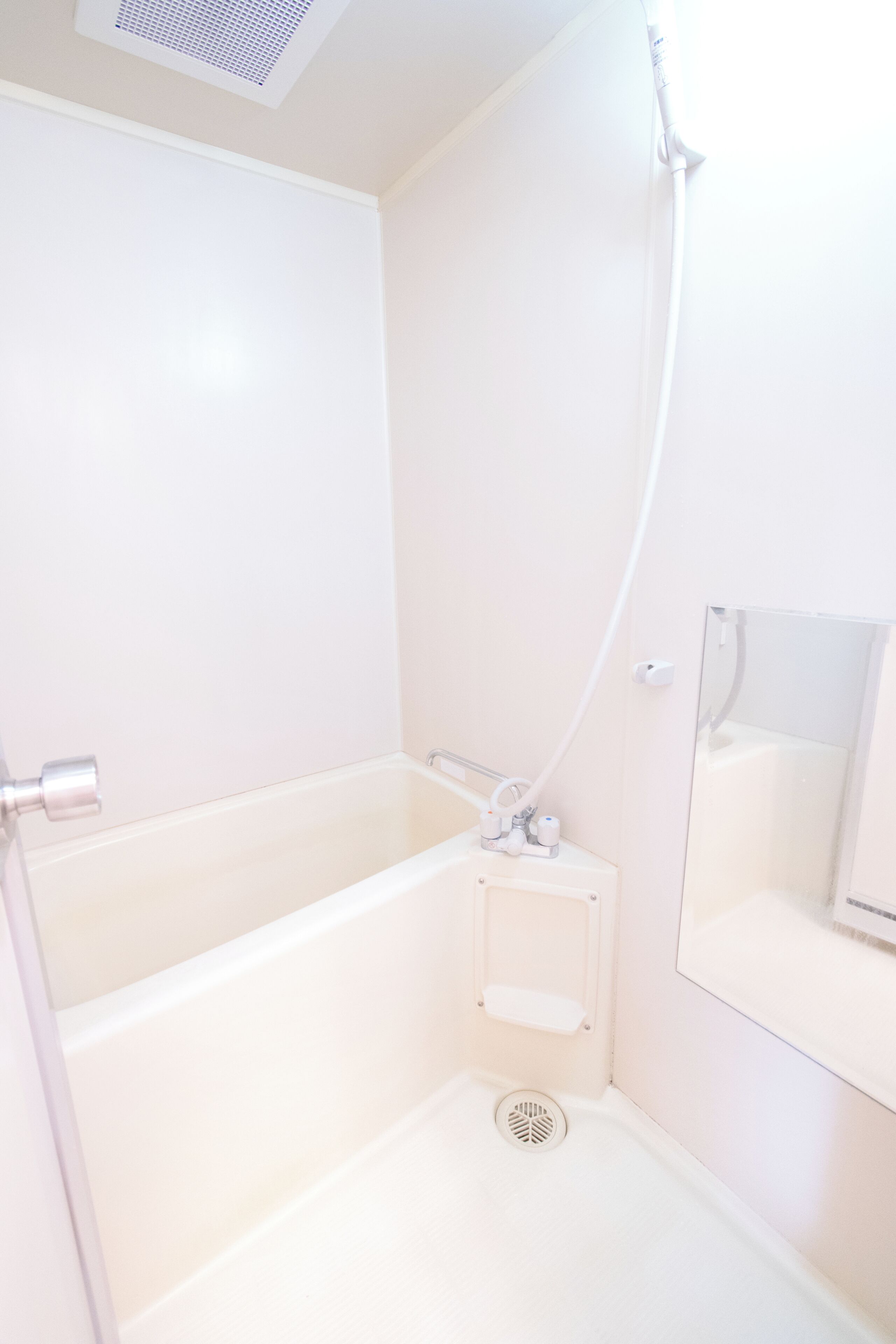 A white bathroom with a bathtub, a shower, a mirror, and a shelf with toiletries.
