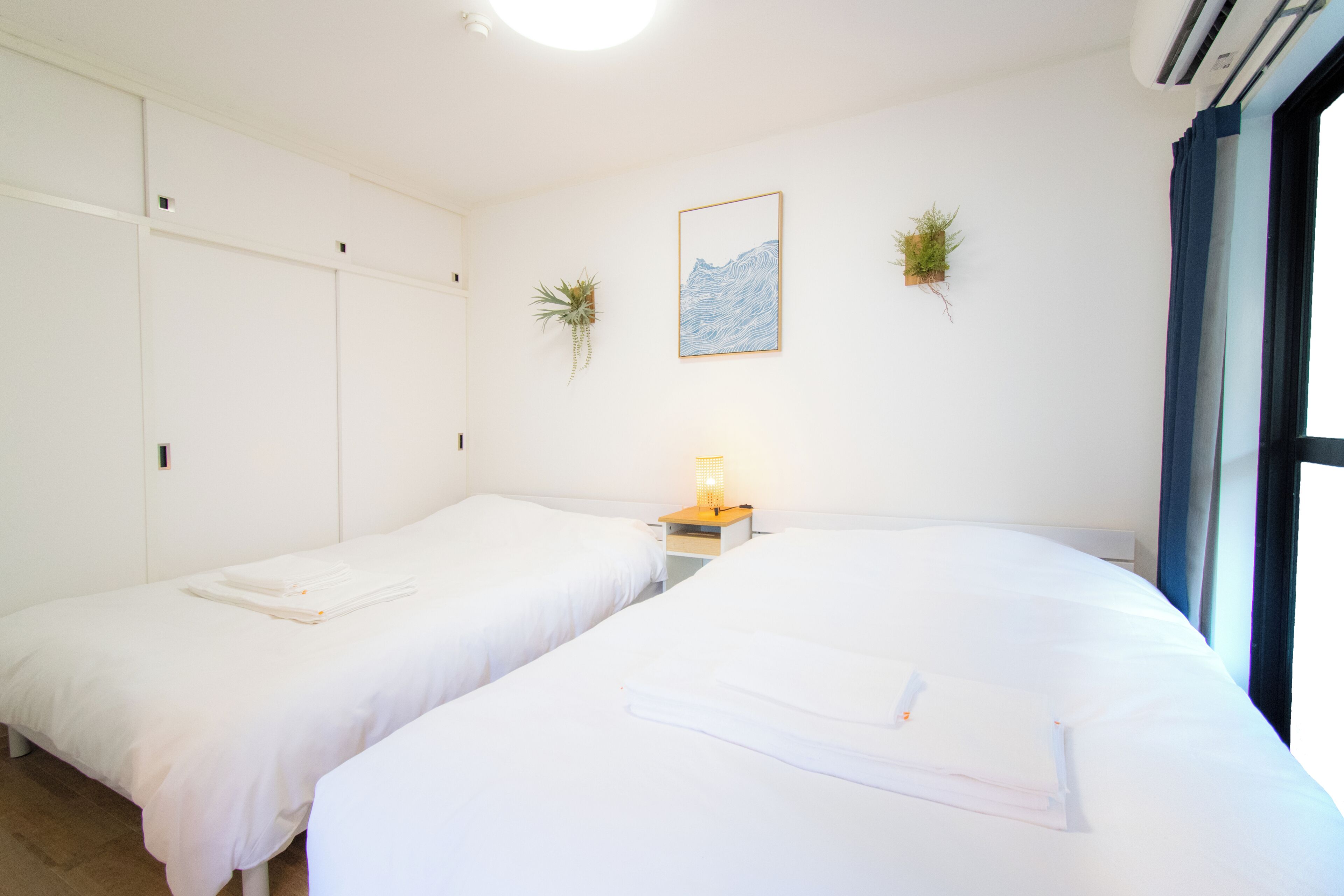 A hotel room with two beds, a nightstand with a lamp, a framed picture on the wall, and a window with curtains.