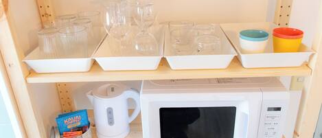 A kitchen shelf with glassware, a kettle, a microwave, and a coffee packet.