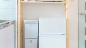 A compact kitchen with a microwave, a small refrigerator, and a shelf with kitchenware. - Kobayashi Building 302 (Tokyo)