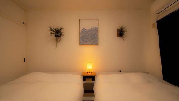A hotel room with two beds, a nightstand with a lamp, and wall-mounted plants. - Kobayashi Building 302 (Tokyo)