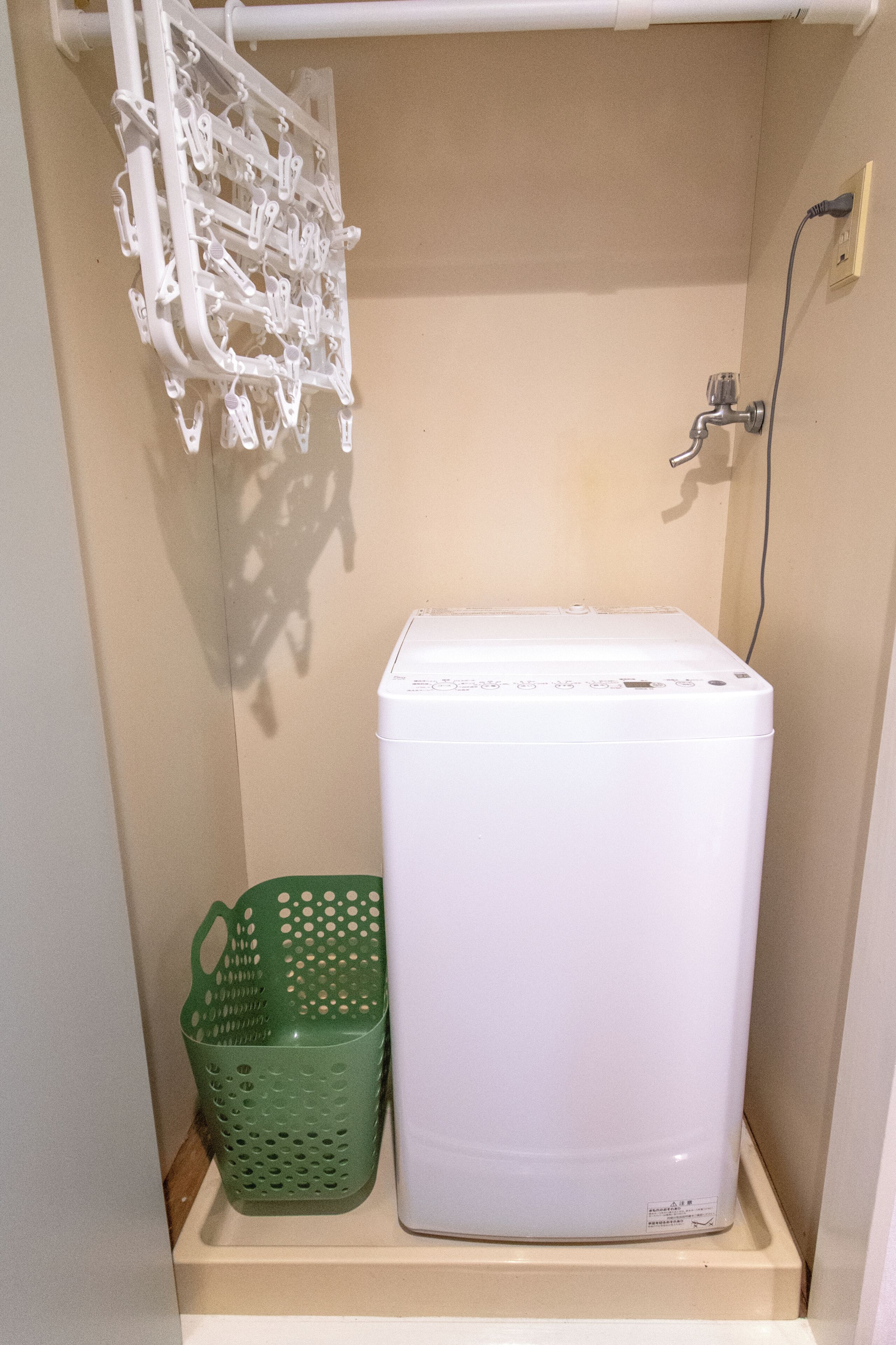 Une buanderie avec un lave-linge blanc, un panier vert et un étendoir.