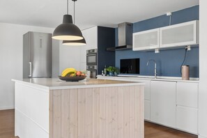 A modern kitchen with a central island, stainless steel appliances, and a blue accent wall. - Lovely holiday home near beach and nature (Vejby)