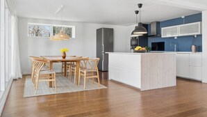 Una cocina moderna con armarios blancos, una isla central y un comedor con sillas y una mesa de madera.