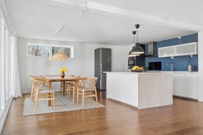 A modern kitchen with white cabinetry, a central island, and a dining area with wooden chairs and a table. - Lovely holiday home near beach and nature (Vejby)