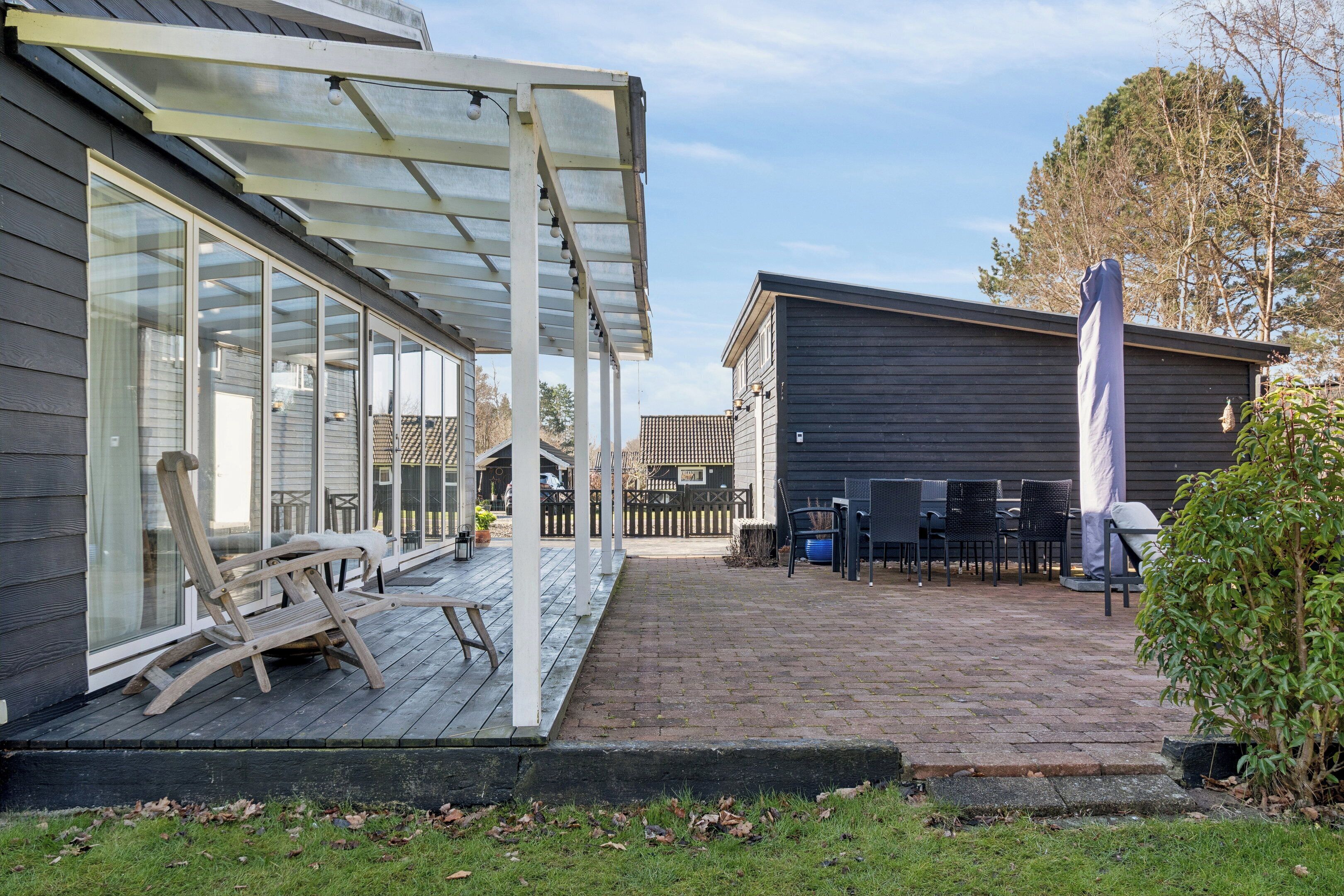 A covered patio with a wooden deck, outdoor furniture, and a glass enclosure.