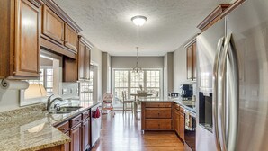 Una cocina con armarios de madera, un refrigerador de acero inoxidable, encimeras de granito y un comedor con una mesa y sillas.