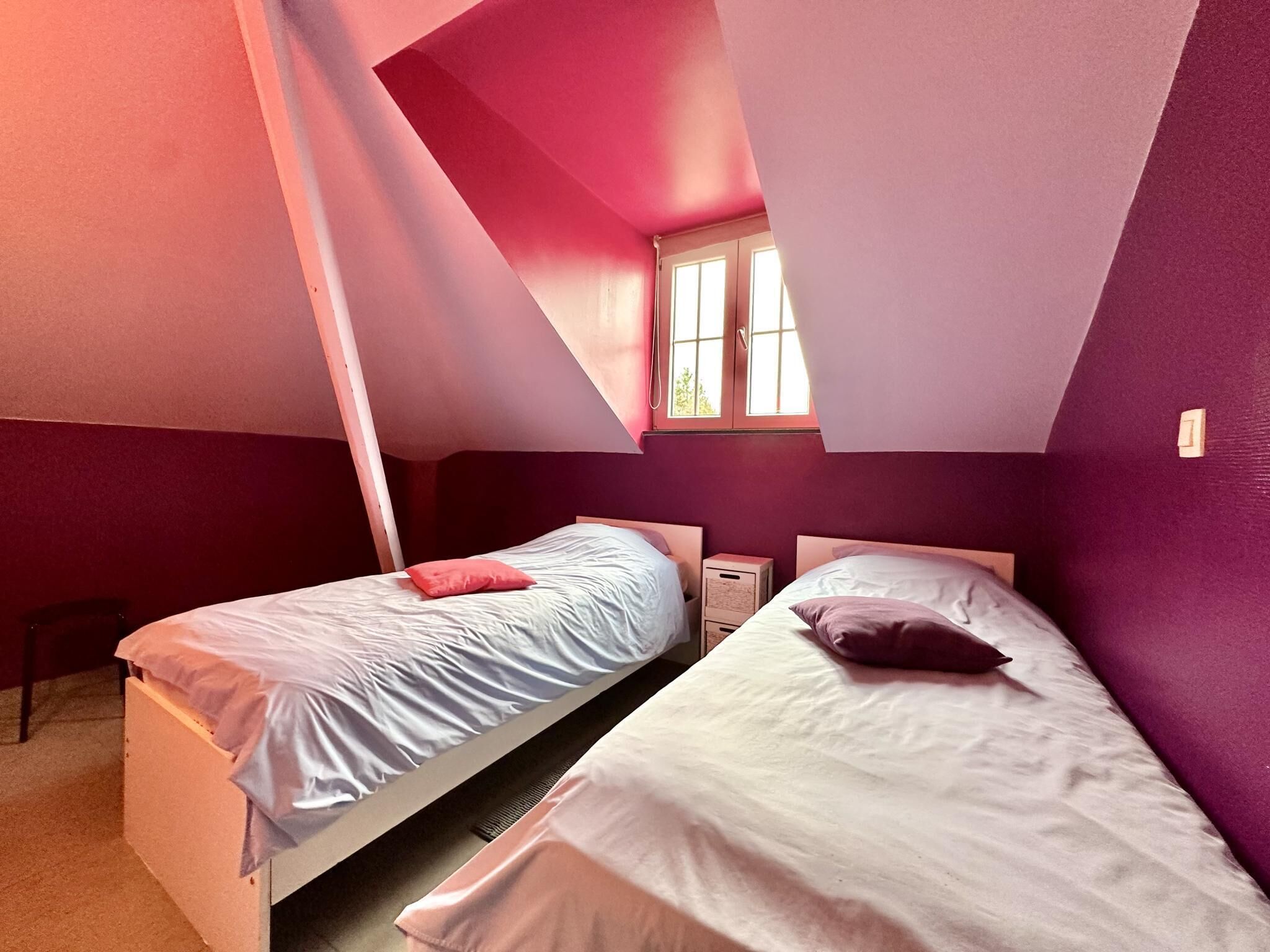 Une chambre avec deux lits, une fenêtre et un plafond en pente.