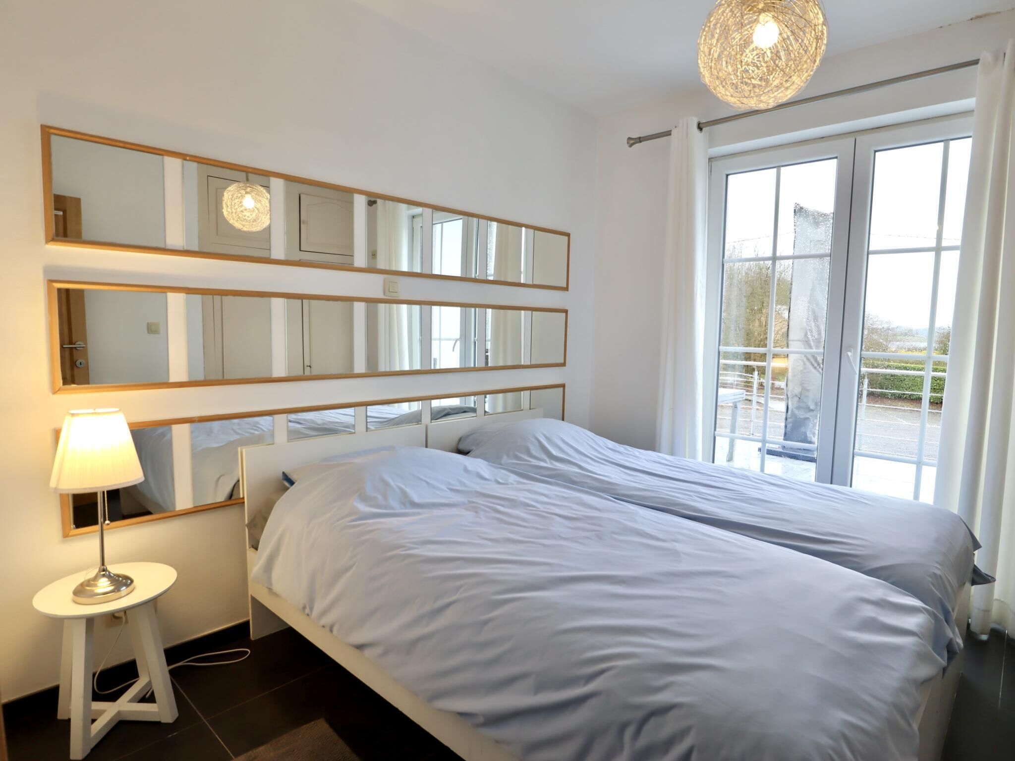 Una camera d'albergo con un letto, una lampada da comodino, uno specchio grande e vista dalla finestra.