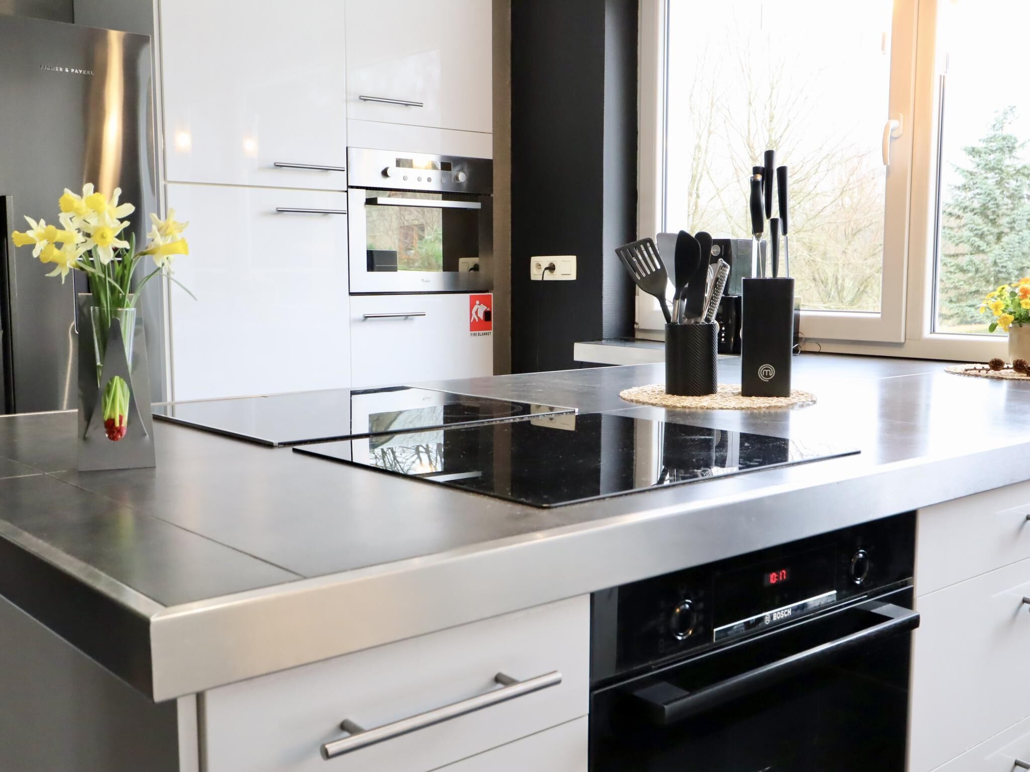 A modern kitchen with a black induction cooktop, stainless steel appliances, and a window with a view of trees.