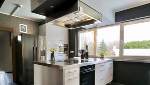 Une cuisine moderne équipée d’un four encastré, d’un réfrigérateur et d’une fenêtre donnant sur les arbres.