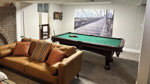 Ein Wohnzimmer mit Billardtisch, braunem Ledersofa, Kamin und Dartscheibe.