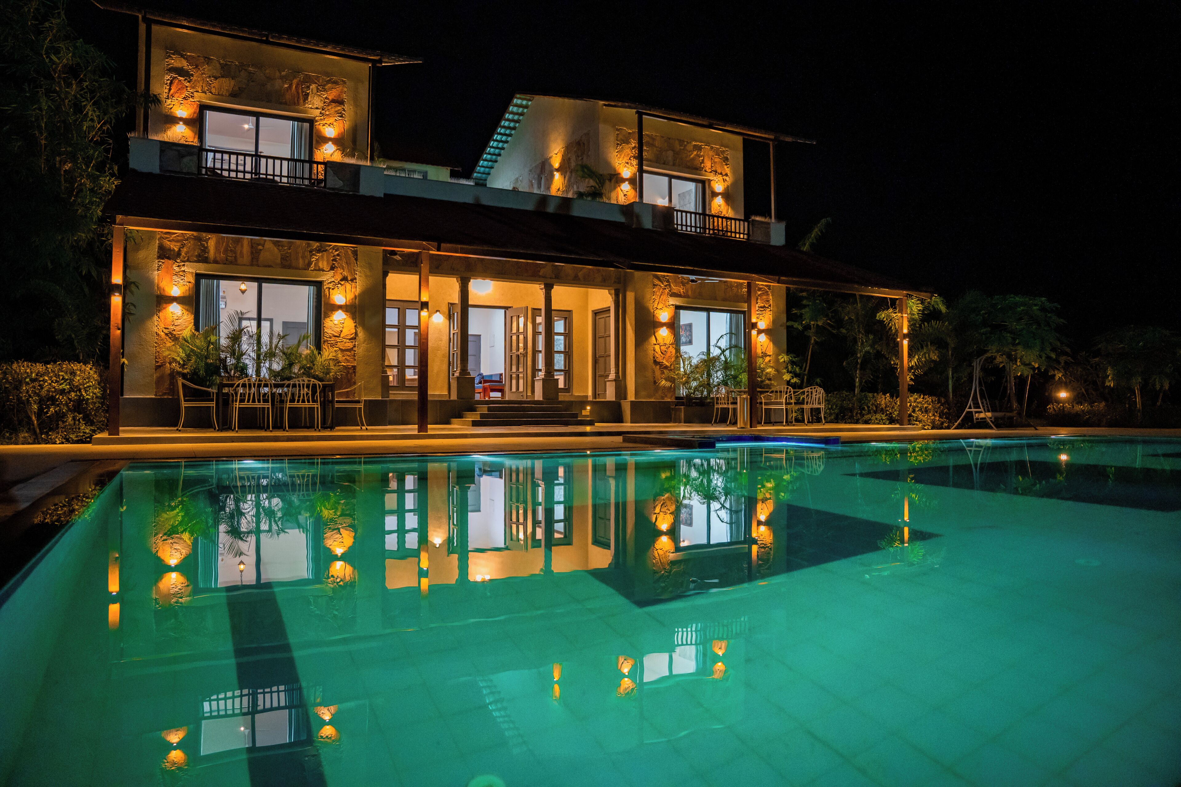 Un edificio de dos pisos con piscina frente a él, ventanas grandes e iluminación exterior.