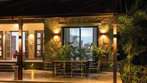 An outdoor seating area with chairs and a table, surrounded by plants and a stone wall. - Alaya Stays Aravale Farm 4BHK Petfrndly (Sohna)