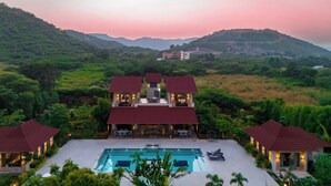 A large house with a swimming pool, surrounded by lush greenery and hills. - Alaya Stays Aravale Farm 4BHK Petfrndly (Sohna)