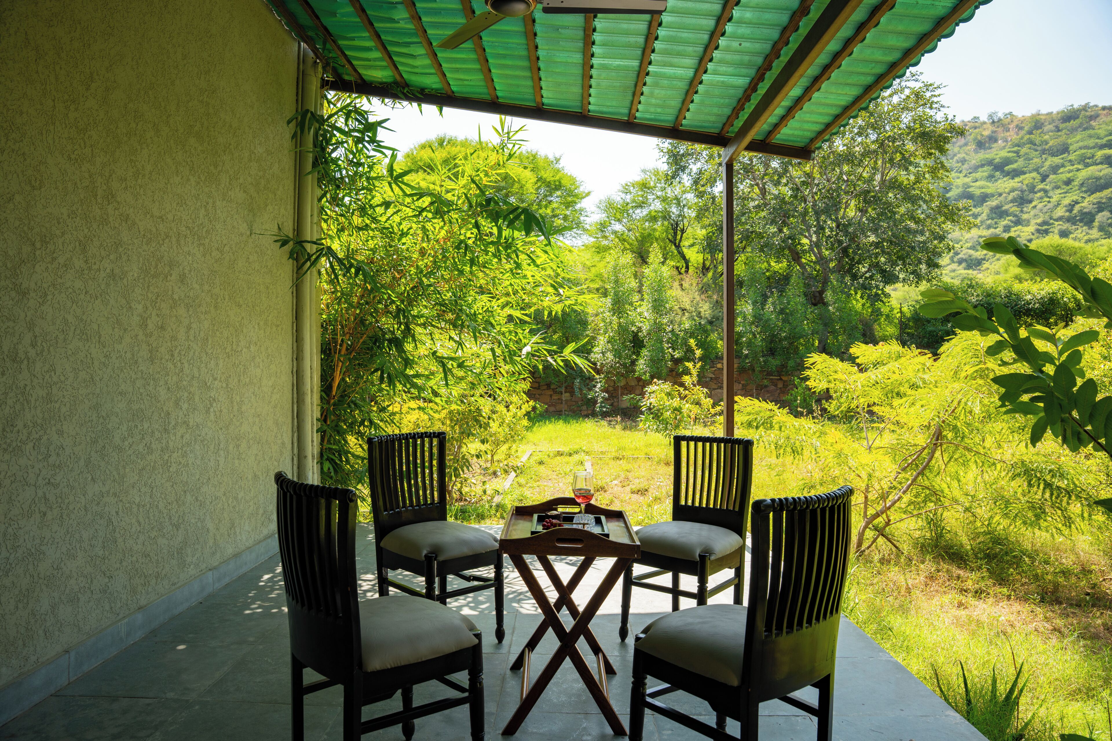A covered patio with four chairs and a table, overlooking a lush green landscape.