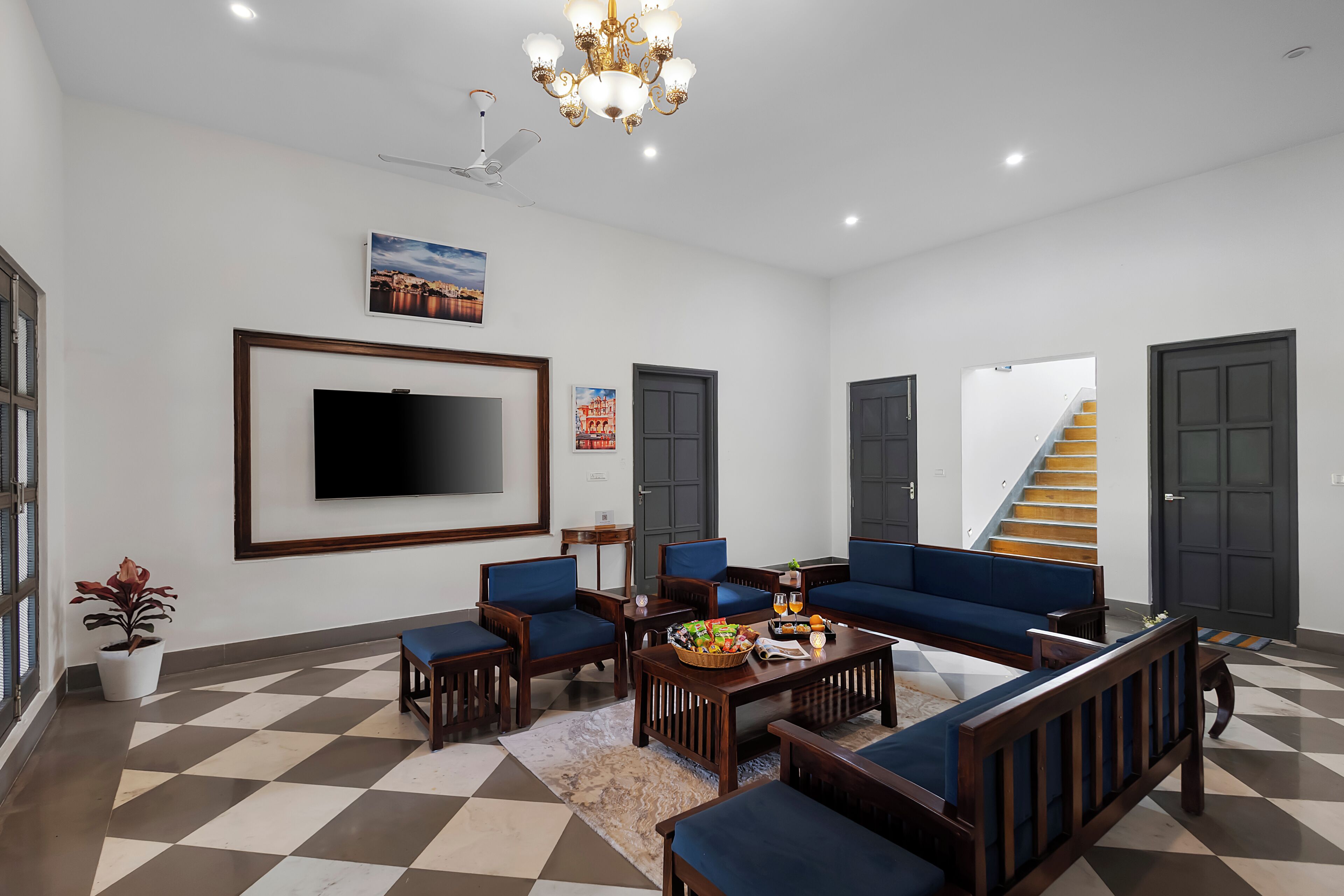 A spacious living room with a large flat-screen TV, blue sofas, wooden furniture, and a staircase leading to another level.