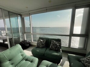A room with a large window overlooking the sea, green upholstered chairs, and a view of the coastline. - Palmetto Sunset Laguito 3-Bedroom Oceanfront (Cartagena)