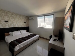 A hotel room with a bed, a desk, a chair, a window with a city view, and a patterned wall. - Palmetto Sunset Laguito 3 habitationes frente al mar (Cartagena)