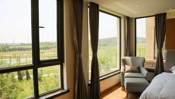 A hotel room with large windows, a bed, a chair, and a view of a landscape. - PengLai Mahota Town (Yantai)