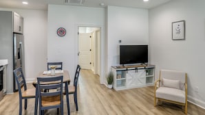 Una cocina moderna con refrigerador integrado, una mesa de comedor con sillas, un televisor sobre un mueble bajo y una zona de estar con un sillón.