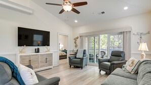 Ein Wohnzimmer mit Deckenventilator, Flachbildfernseher, Schrank, Sofa und Sessel.